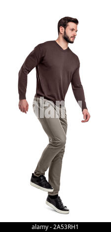 A serious looking man in casual clothes walks down invisible stairs on a white background. Stock Photo