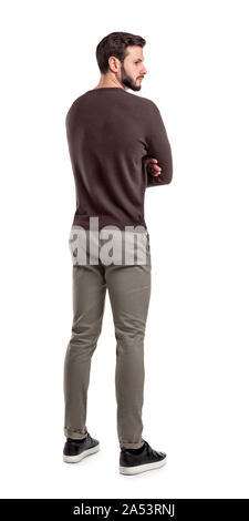An adult bearded man in casual sweater stands in a back view half turned to look behind his shoulder. Stock Photo