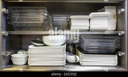 Old stainless steel industrial kitchen cabinet with stacks of square plates and kitchenware Stock Photo