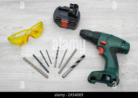 A cordless drill set on a wooden table background with a set of bits in the box and yellow protective glasses around. Stock Photo