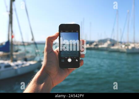 Person with a smartphone taking a picture of boats in the sea with the beautiful sky in background Stock Photo
