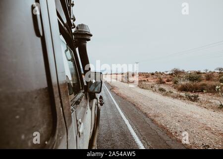 Closeup shot of an old car driving on the road surrounded by green bushes under the clear sky Stock Photo