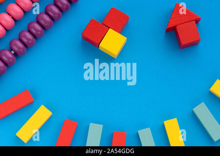 Frame from kids toys, top view on children's educational games on blue paper background. Multicolored wooden bricks, abacus, house from building blocks, pyramide. Flat lay, copy space for text. Stock Photo