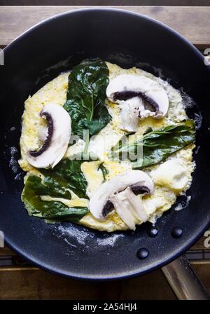 Omelette with spinach and mushrooms in a pan close-up on the table. Stock Photo