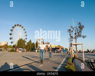 Novosibirsk, Russia - 08.25.2019: Scooters and skaters against two large ferris wheels in the park on Mikhailovskaya embankment after reconstruction a Stock Photo