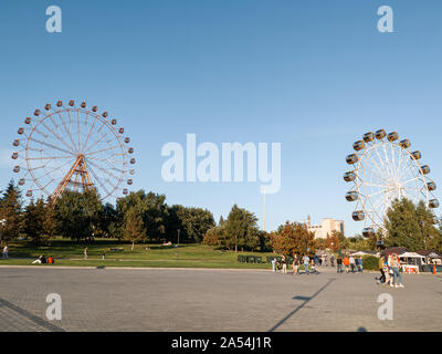 Novosibirsk, Russia - 08.25.2019: Two large ferris wheels in the park on Mikhailovskaya embankment after reconstruction against a blue sky and people Stock Photo