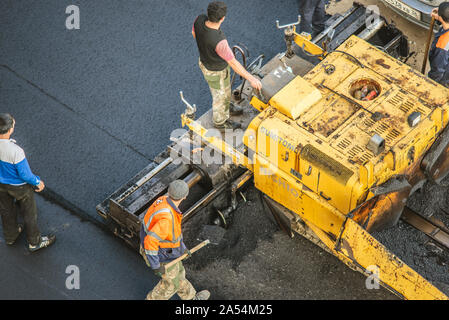 Workers lay a new asphalt coating using hot bitumen. Work of heavy machinery and paver. The view from the top Stock Photo