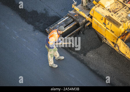 Workers lay a new asphalt coating using hot bitumen. Work of heavy machinery and paver. The view from the top Stock Photo