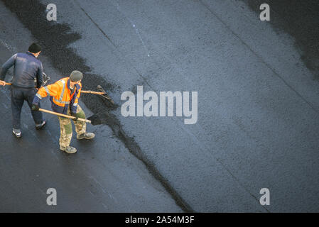Workers lay a new asphalt coating using hot bitumen. Work of heavy machinery and paver. The view from the top Stock Photo
