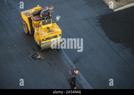 Workers lay a new asphalt coating using hot bitumen. Work of heavy machinery and paver. The view from the top Stock Photo