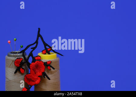 Needlework concept. Two large spools of thread and needles on a blue background. The photo has an application in the form of red flowers. Plenty of ro Stock Photo