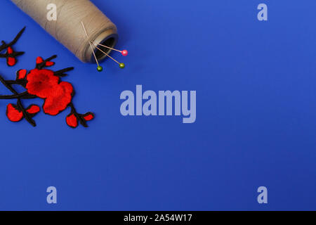 Needlework concept. One large spool of thread and needles on a blue background. The photo has an application in the form of red flowers. Plenty of roo Stock Photo