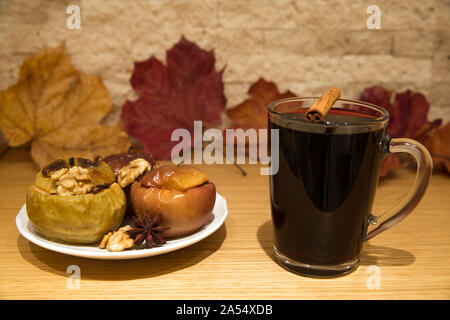 Hot mulled wine and baked apples with spices, walnuts, cinnamon sticka, cloves and anise stars, autumn scene with colorful dried leaves on bricks wall Stock Photo