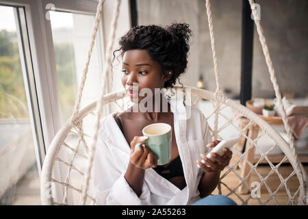 Curly woman looking into window while enjoying coffee Stock Photo