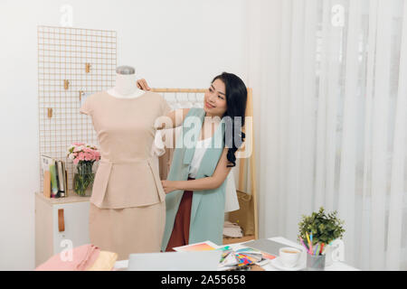 An Asian girl  is working in the workshop studio. She makes fitting on the dress on the mannequin. Stock Photo