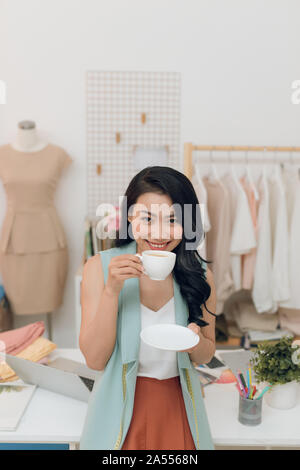 Young fashion designer on her atelier making a pause and drinking coffee Stock Photo