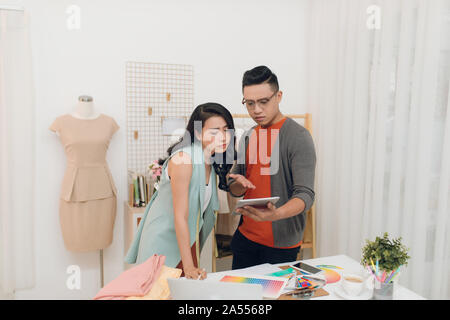 Two young woman and man fashion designers working and using tablet together at the studio Stock Photo