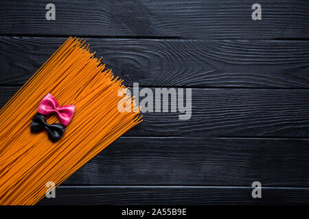 Orange tomato spaghetti and big huge black and pink farfalline on black wooden background. Copy space. Stock Photo