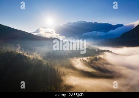 Sunrise, sunbeams in fog over forest at Ferchensee, Karwendel Mountains in the back, near Mittenwald, aerial view, Werdenfelser Land, Upper Bavaria Stock Photo