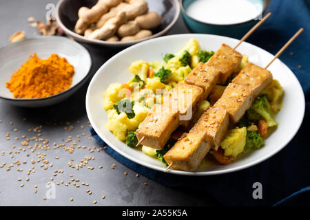 Tofu satay with stir fried vegetables, spices and seeds in a dish on a stone background Stock Photo