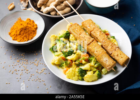 Tofu satay with stir fried vegetables, spices and seeds in a dish on a stone background Stock Photo