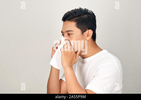 Closeup of sick Asian man blowing nose into tissue, suffering from common cold. Medical and healthcare concept on white background Stock Photo