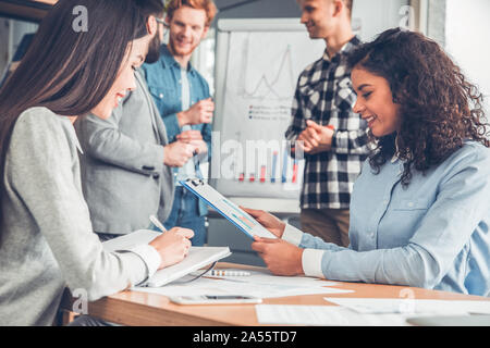 Startupers working together at office women sitting at table looking at documents taking notes joyful Stock Photo