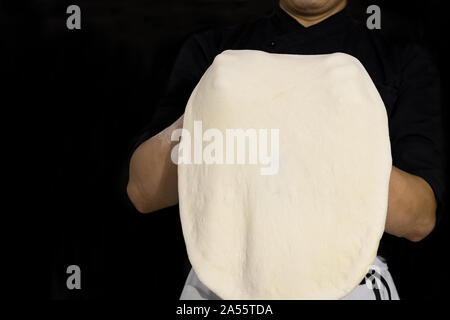 Chef preparing dough for pizza rolling with hands isolated in black background. Stock Photo
