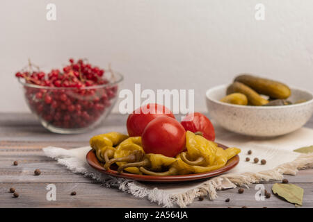 Homemade pickled peppers and tomatoes on a ceramic plate on a linen napkin. Near pickles and viburnum in bowls Stock Photo