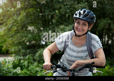Woman riding a bicycle in the city street outdoor. Portrait of happy middle aged female 40 45 years old wearing a bike helmet Stock Photo