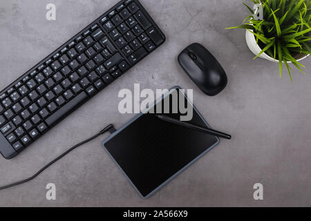Working place on dark table with copy space. Keyboard, computer mouse, pen, graphics tablet, flower in pot. Flat lay. Top view of blackboard office de Stock Photo