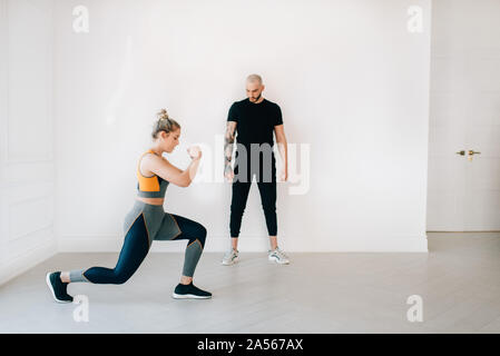 Fitness instructor observing woman doing lunges in studio Stock Photo