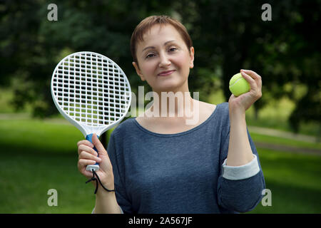 Woman playing tennis. Portrait of active middle aged woman holding a racket and a tennis ball outdoors Stock Photo