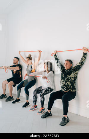 Friends doing squat against wall with resistance band Stock Photo