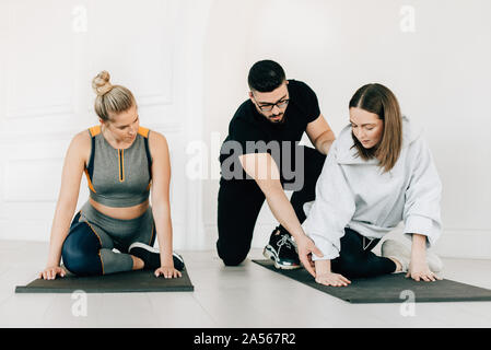 Fitness instructor teaching women stretching legs in studio Stock Photo