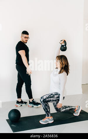 Fitness instructor observing woman doing lunges with kettlebell in studio Stock Photo