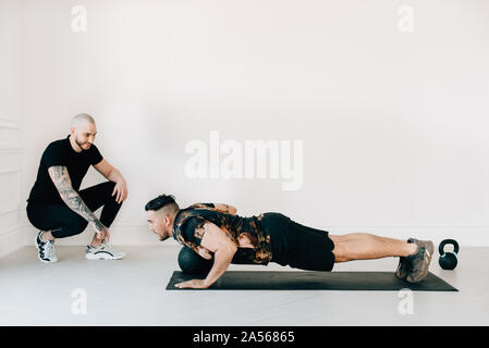 Fitness instructor observing man doing plank with medicine ball in studio Stock Photo