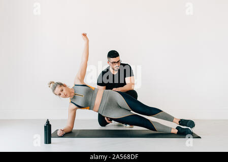 Fitness instructor observing woman doing side plank in studio Stock Photo
