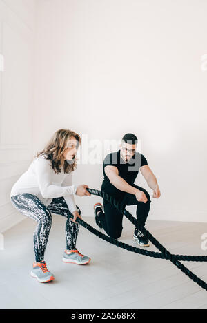 Fitness instructor observing woman using battle rope in studio Stock Photo
