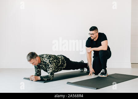 Fitness instructor observing man doing plank in studio Stock Photo