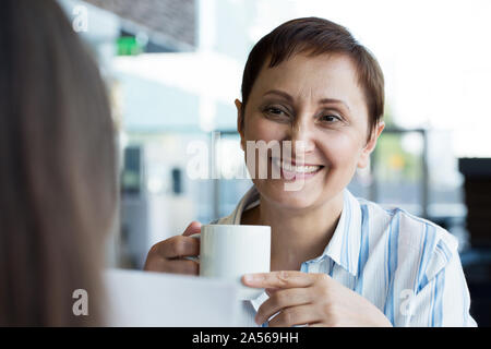 Older woman talking to her colleague. Woman having a meeting with a business partner or a customer. Portrait of middle aged female having coffee / tea Stock Photo