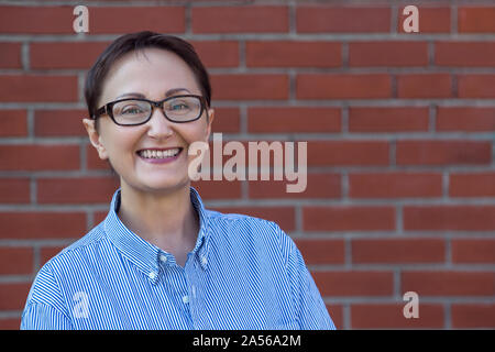 Business woman wearing glasses and shirt on a blurred brick wall background with a copy space on the right. Stock Photo