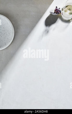 High key still life with glass of white wine and white plate on white table, overhead view Stock Photo