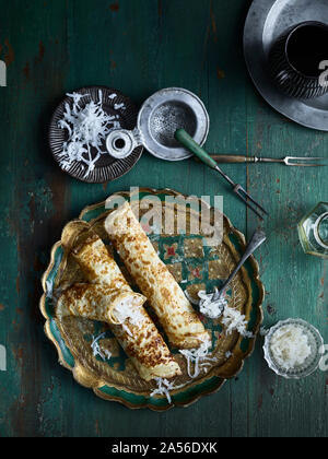 Rustic low key still life with plate of grated coconut pancakes on table, overhead view Stock Photo
