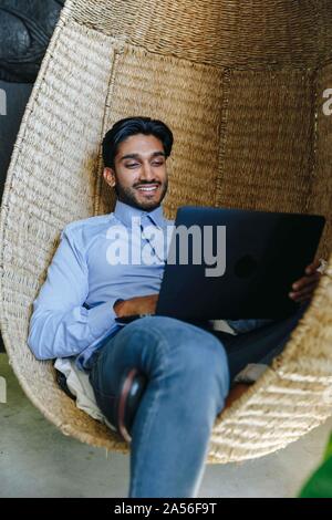Businessman using laptop on cane swing chair Stock Photo