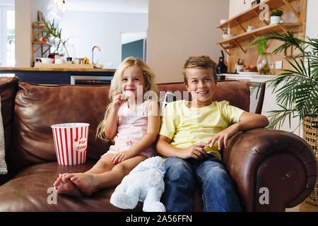 Children relaxing with popcorn on sofa at home Stock Photo
