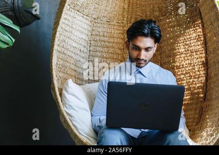 Businessman using laptop on cane swing chair Stock Photo