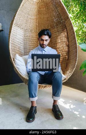 Businessman using laptop on cane swing chair Stock Photo