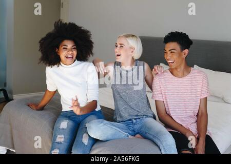Young man and two female friends sitting on bed laughing Stock Photo