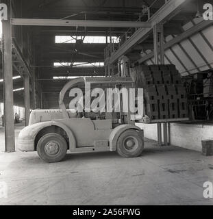 1950s, historical, a male worker operating an electric fork-lift truck as he collects recently fired bricks at the brickworks of the London Brick Company (LBC) at Stewartby, Bedfordshire, England, UK. In this era, the brickworks were the largest in Europe. Stock Photo